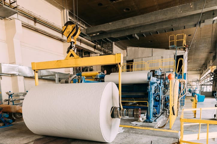 A paper machine winding a finished roll on a mill floor.
