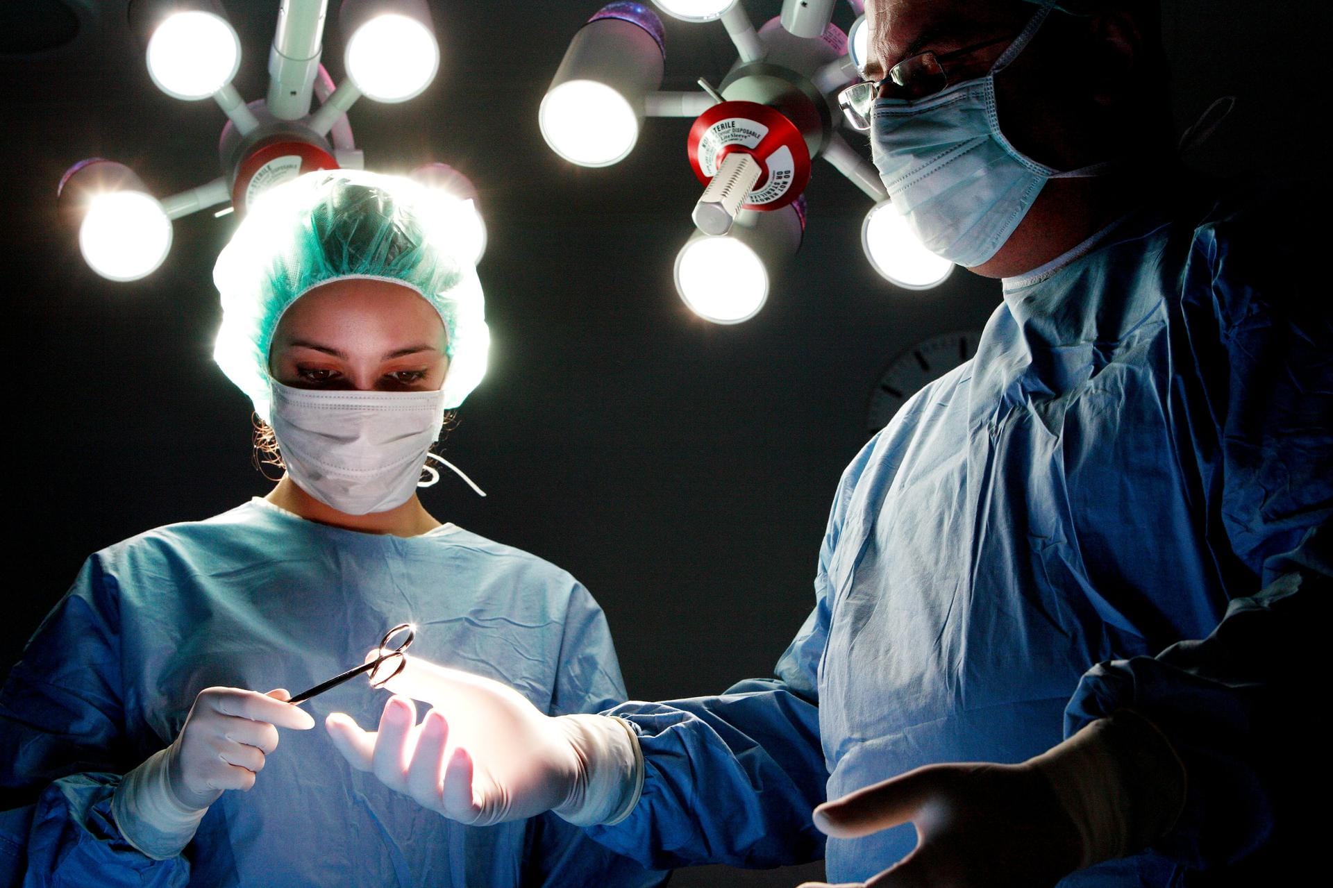 Two surgeons at work under the lights of an operating theatre.