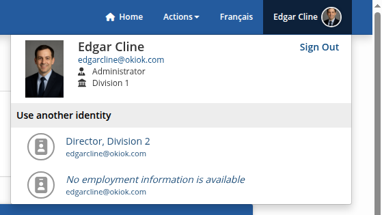The profile menu open in the top right: the signed-in user’s photo, name, email, role and division, a sign-out link, and below them a Use another identity list offering the other identities the same person holds.
