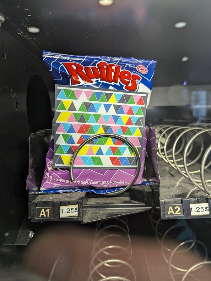 The bag of Ruffles chips from the vending machine, with a paper strip of coloured triangles attached to it.